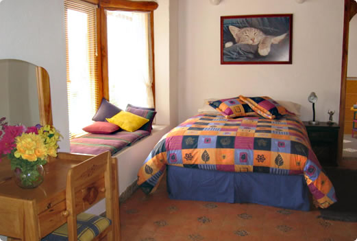 Dormitorio con cama y escritorio junto a la ventana.