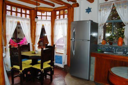 Comedor con mesa de madera y cocina al fondo.